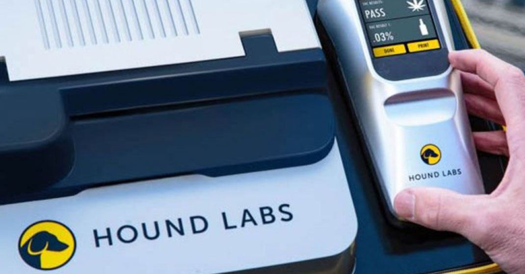 a silver fax machine looking device with a phone attachment with an led screen. the machine reads hound labs. the led screen show a marijuana leaf and the word PASS.