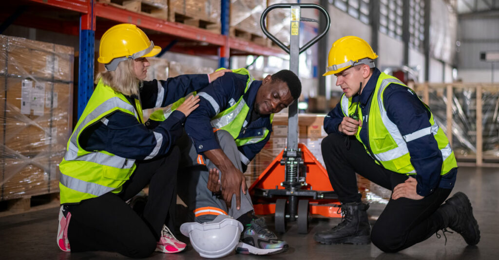 two people attend to a hurt worker in a factory.